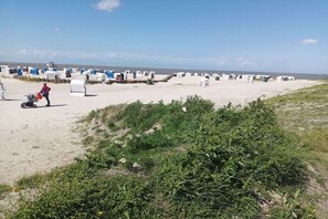 A beach with beach huts and a person pushing a stroller. - Dreaming by the fireplace (Wangerland)