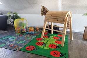 A child's play area with a wooden playhouse, a colorful play mat, and toys. - Dreaming by the fireplace (Wangerland)