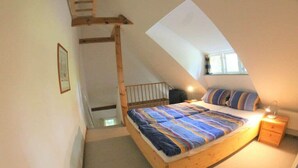 Een slaapkamer met een schuine plafond, een houten bedframe, een nachtkastje en een raam dat natuurlijk licht biedt.