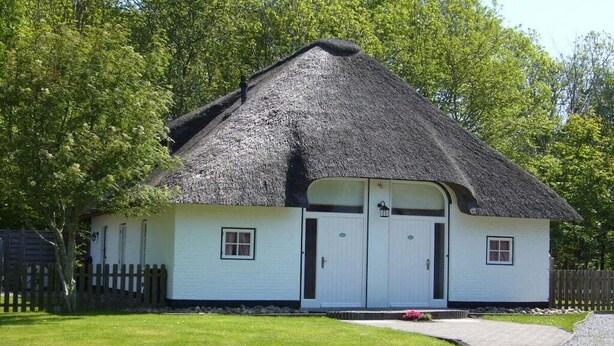 Een rieten huisje met een witte gevel, twee deuren en een klein portaal.