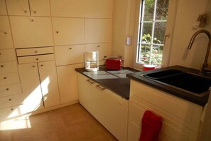 Eine Küche mit weißen Schränken, einer schwarzen Arbeitsplatte, einem roten Toaster und einem Fenster mit Blick auf Grünflächen.