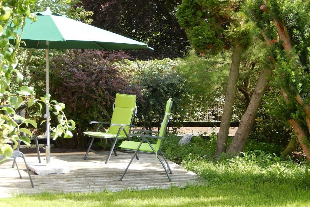 Eine Terrasse im Freien mit zwei grünen Stühlen und einem grünen Sonnenschirm.