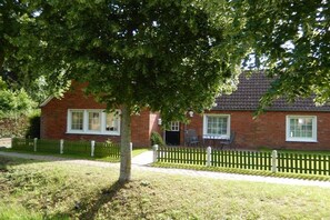 Ein Ziegelhaus mit weißem Zaun, einem gepflasterten Weg und einem Baum, der Schatten spendet.