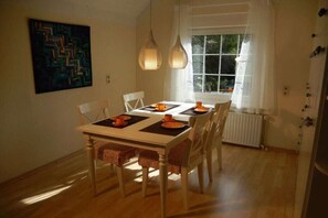 Un coin repas avec une table dressée pour quatre personnes, une fenêtre avec des rideaux et un radiateur.