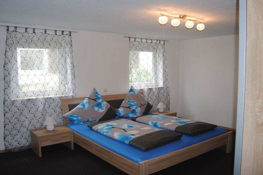 Une chambre à coucher avec un lit double, deux tables de chevet, une lampe, des rideaux et un luminaire au plafond.