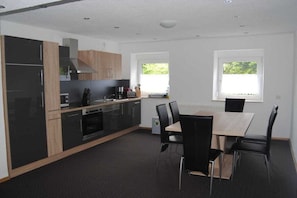 A modern kitchen with black cabinets, a wooden countertop, and a dining area with a table and chairs. - Holiday apartment in Kötz with Wi-Fi (Kötz)