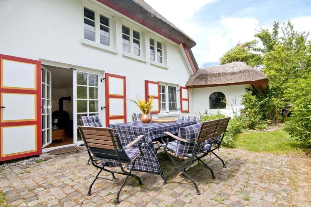 Une maison avec un patio, une table et des chaises, et une structure dotée d’un toit de chaume.