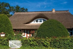 Ein traditionelles Haus mit Strohdach und weißem Zaun, umgeben von gepflegten Hecken.