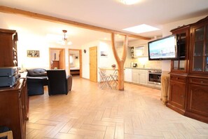 A spacious living area with a herringbone floor, a television mounted on the wall, and a kitchen with wooden cabinets and a stove. - 3-room apartment near the harbor - ground floor with terrace (Zingst)