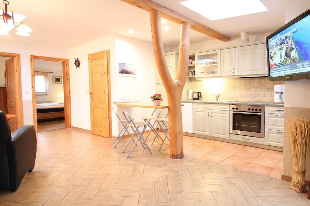 A modern kitchen with wooden beams, a dining area with a table and chairs, and a television mounted on the wall.
