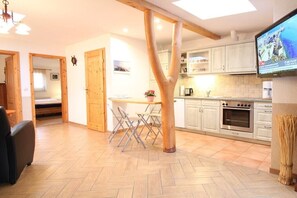 A modern kitchen with wooden beams, a dining area with a table and chairs, and a television mounted on the wall. - 3-room apartment near the harbor - ground floor with terrace (Zingst)