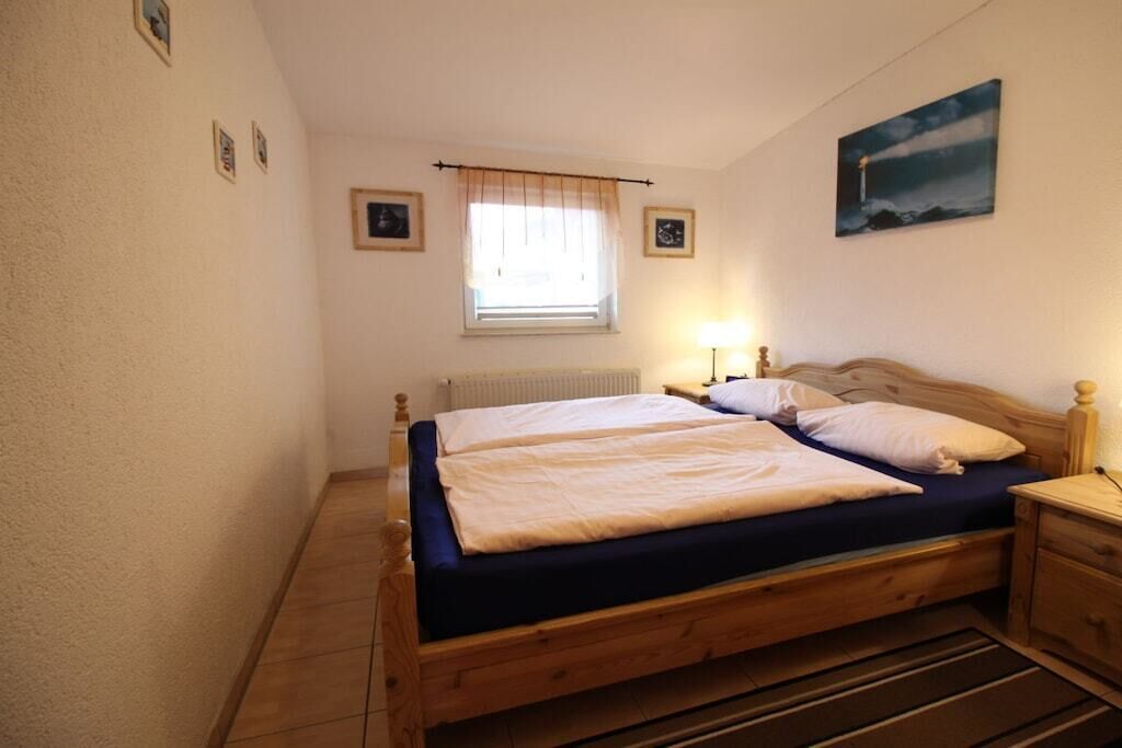 Ein Schlafzimmer mit einem Doppelbett, einem Nachttisch, einer Lampe, einem Fenster mit Vorhang und einem Wandbild.