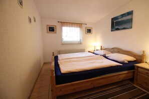 Une chambre à coucher avec un lit double, une table de chevet, une lampe, une fenêtre avec un rideau et un tableau accroché au mur.