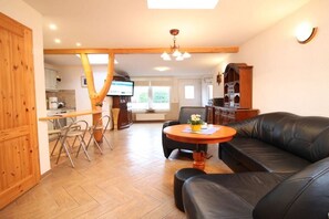 A cozy living room with a black leather sofa, a wooden dining table, and a kitchen area with a TV. - 3-room apartment near the harbor - ground floor with terrace (Zingst)