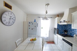 A kitchen with white cabinets, a blue tiled backsplash, a white refrigerator, and a wall clock. - Holiday home with 2 bedrooms (Tavernes, Frankreich)