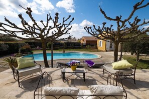 A swimming pool area with lounge chairs and a table, surrounded by trees and a building in the background. - Holiday home with 2 bedrooms (Tavernes, Frankreich)