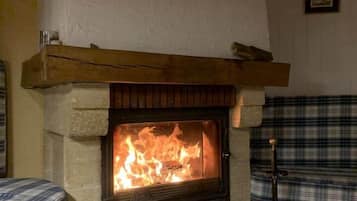 A stone fireplace with a fire, a wooden mantel, and a plaid bench.