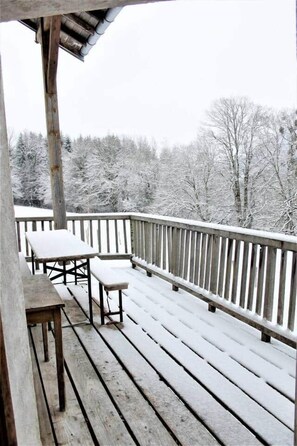 En træterrasse med bænke og gelænder, med udsigt over et sneklædt landskab med træer.