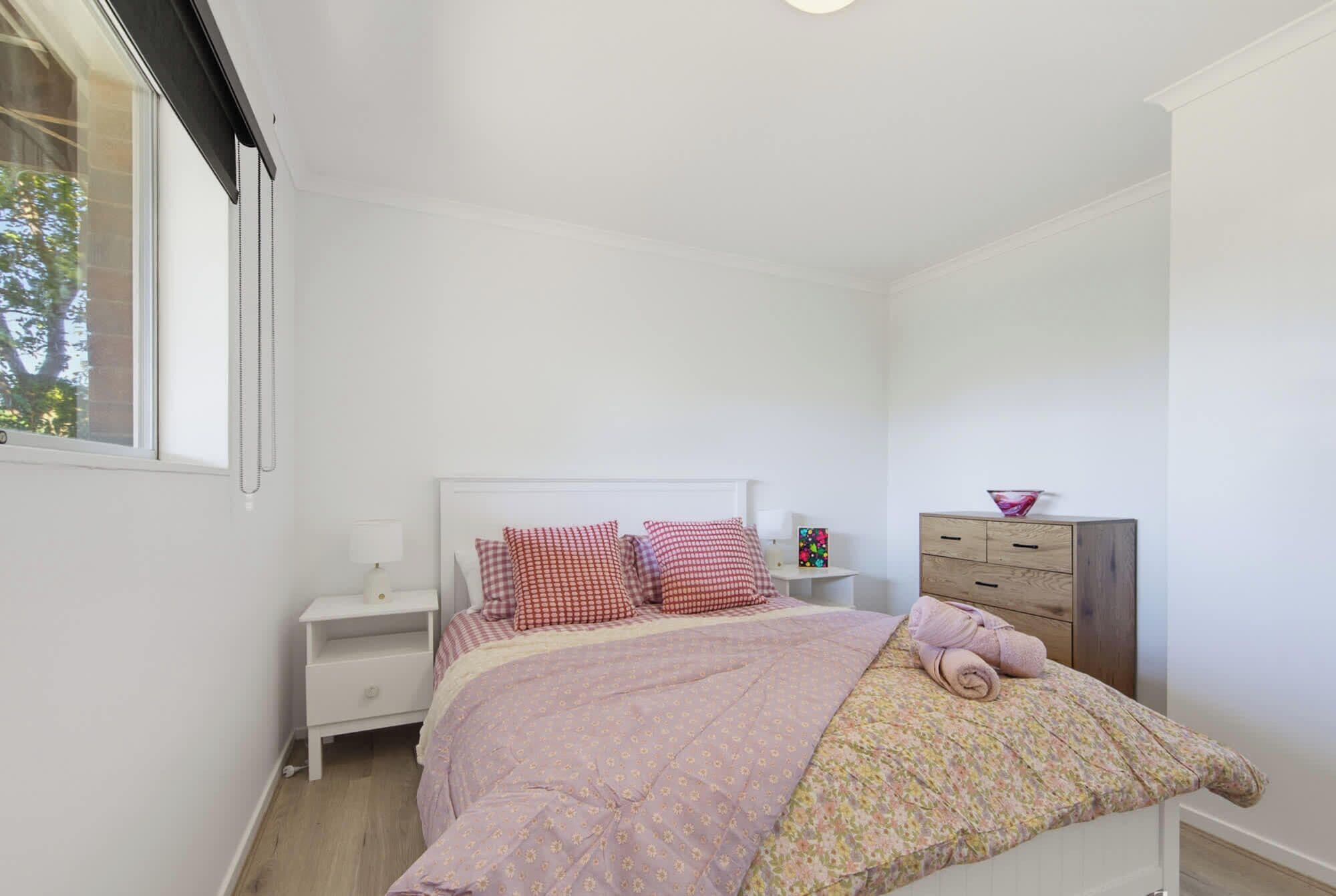 Un dormitorio con cama, mesita de noche, cómoda y ventana.