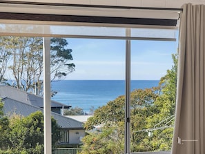 A view through a window with a clear sky and a body of water in the distance. - Coastal Haven | Ocean Views + Pets Welcome. (Denhams Beach)