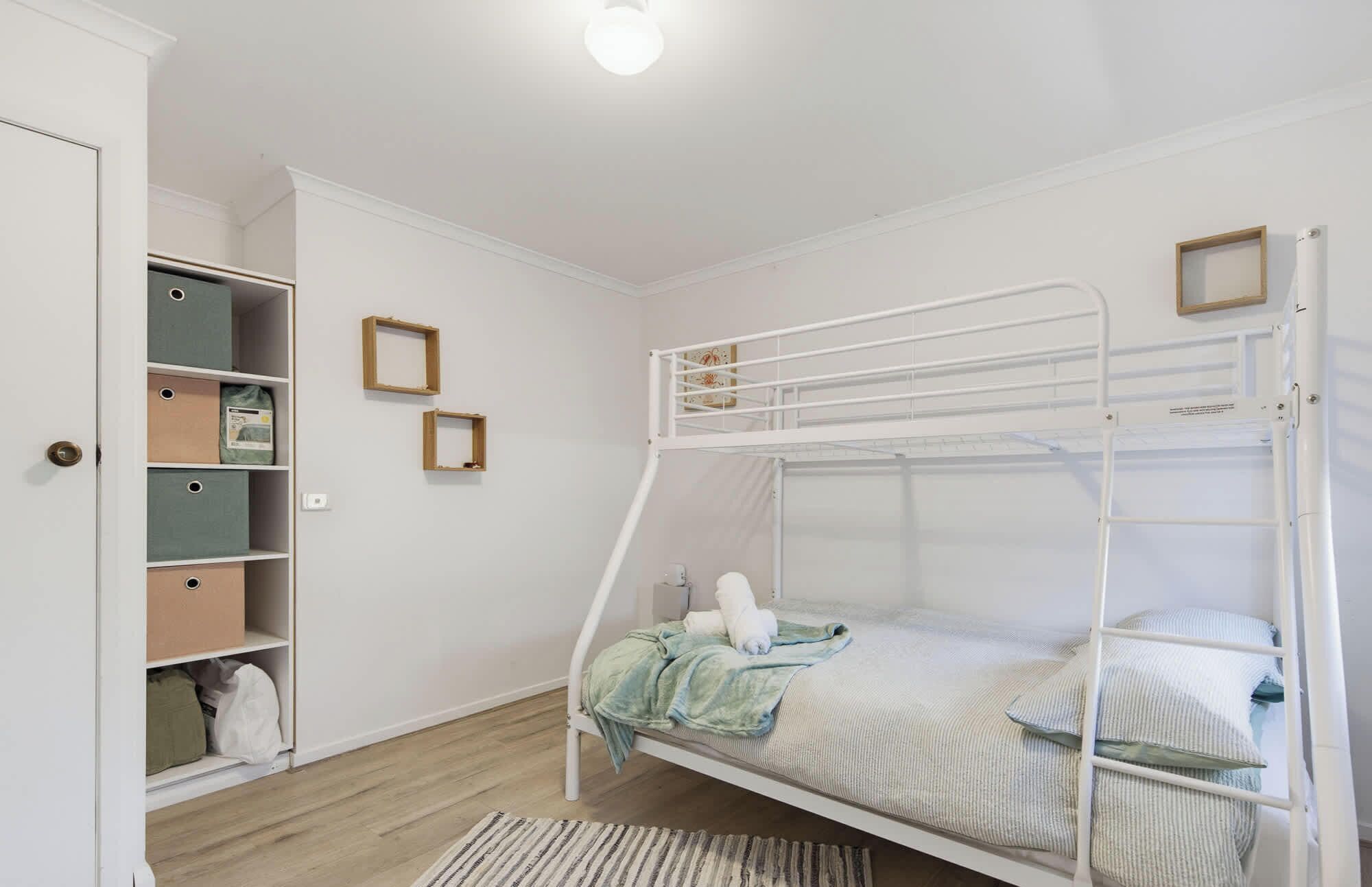 A bunk bed with a white metal frame, a wooden ladder, and a small shelf above it.
