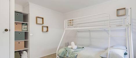 Ein Stockbett mit weißem Metallgestell, einer Holzleiter und einem kleinen Regal darüber.