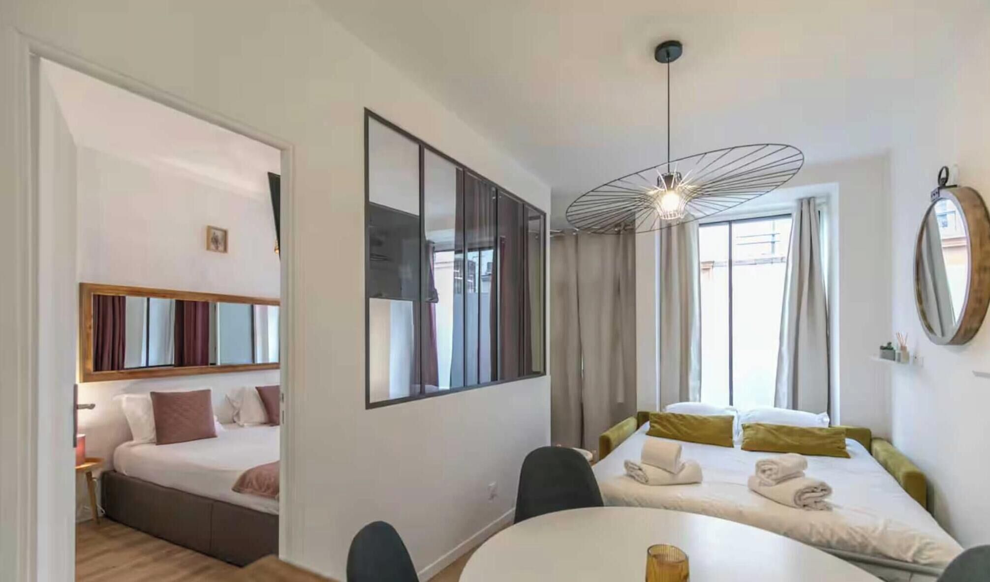 A hotel room with a bed, a desk, a chair, a round table, a mirror, and a ceiling light fixture.