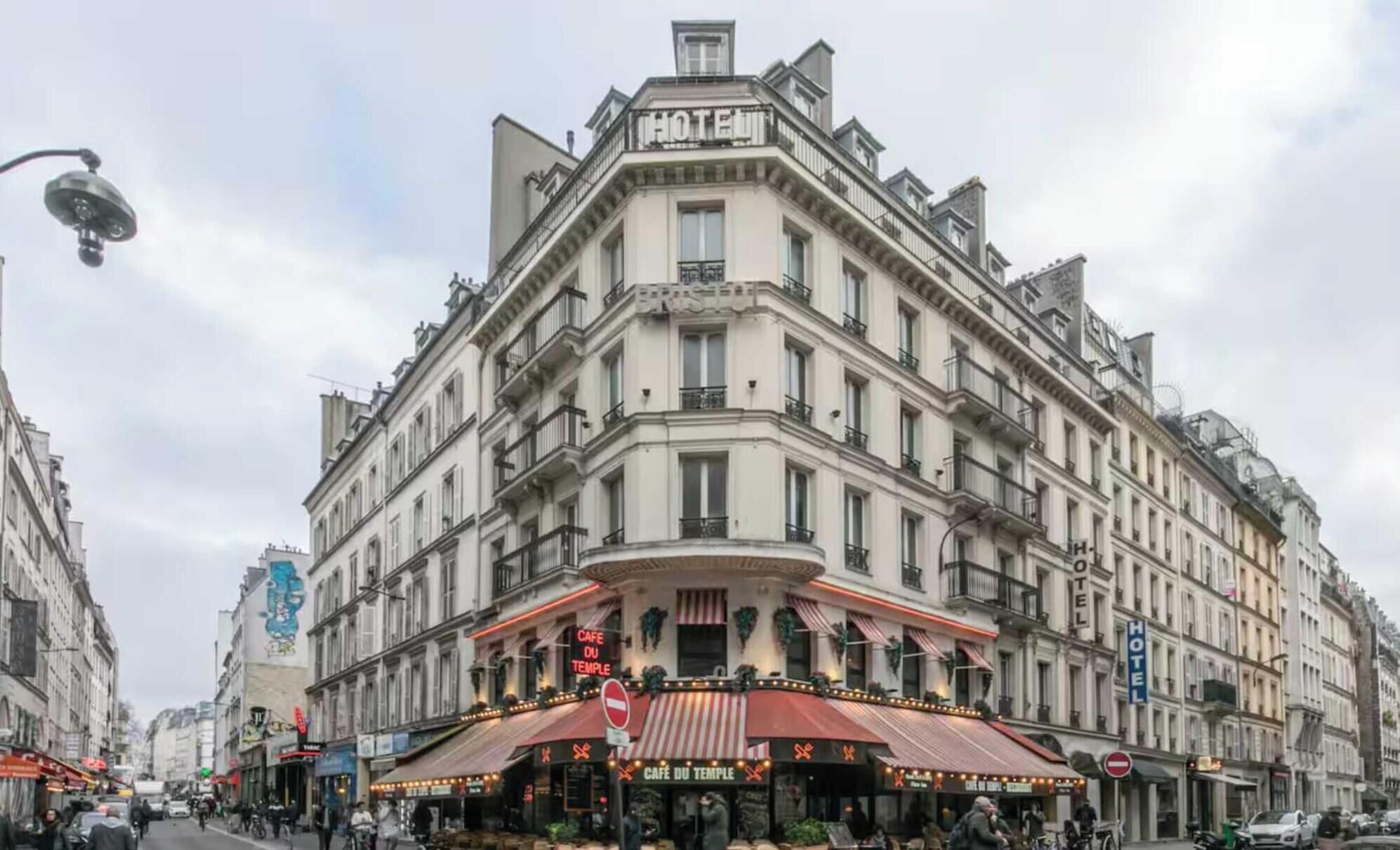 A corner building with a 'HOTEL' sign, a 'CAFE DU TEMPLE' with outdoor seating, and a 'BRIS' sign.