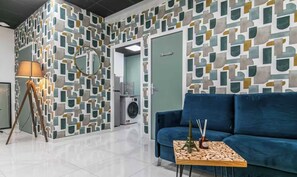 A modern interior with a geometric patterned wall, a blue sofa, a lamp, and a small table with decorative items. - Spacious Apartment -3BR/10P- Montreuil near Paris (Montreuil)