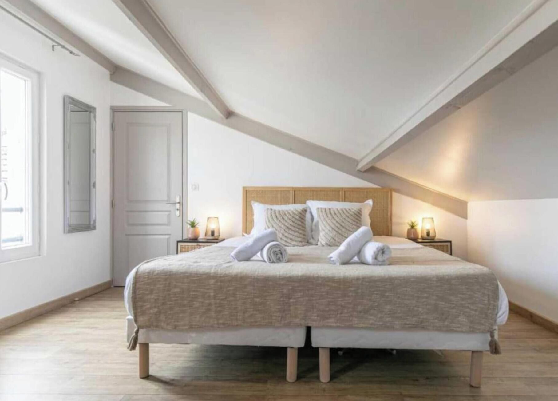 A bedroom with a large bed, two bedside tables with lamps, a wooden headboard, and a sloped ceiling.