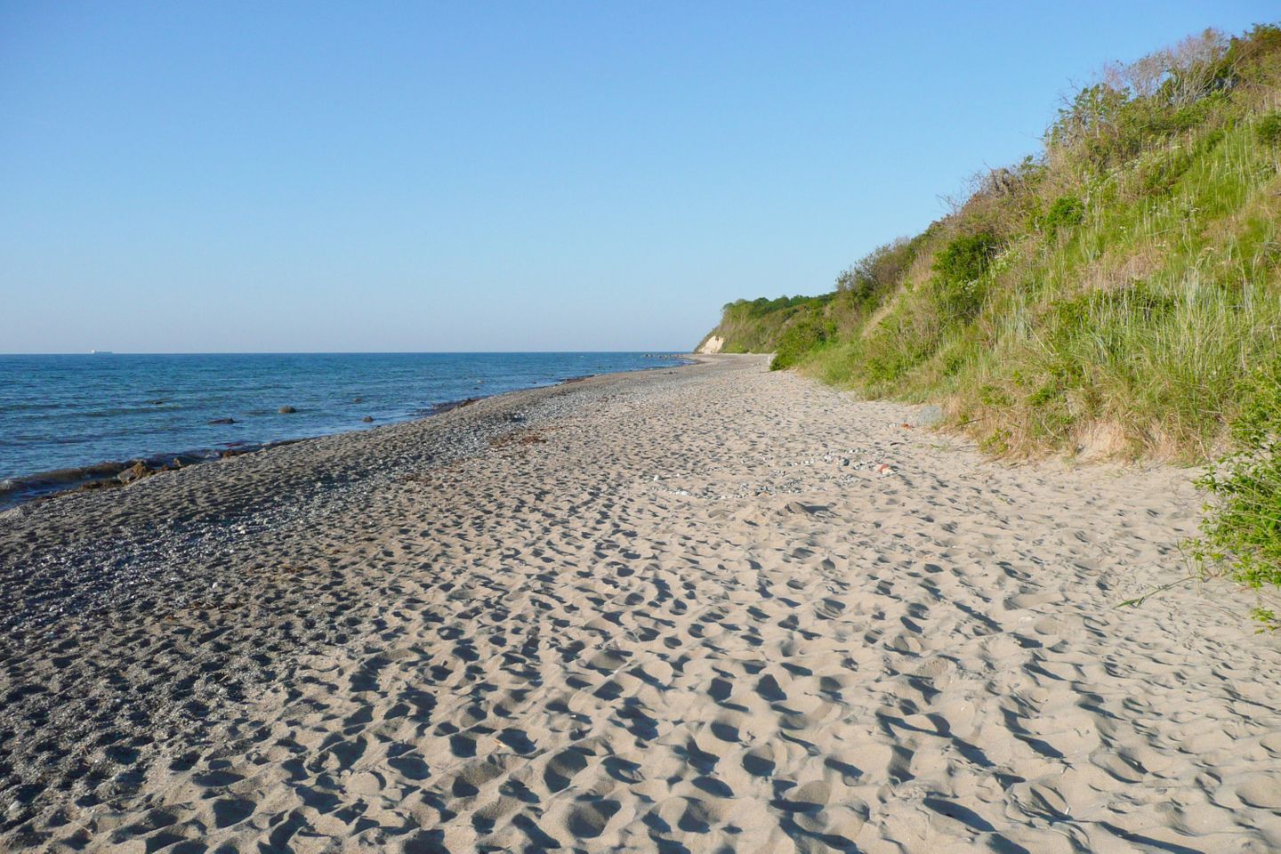 En sandstrand med en klar himmel og roligt hav.