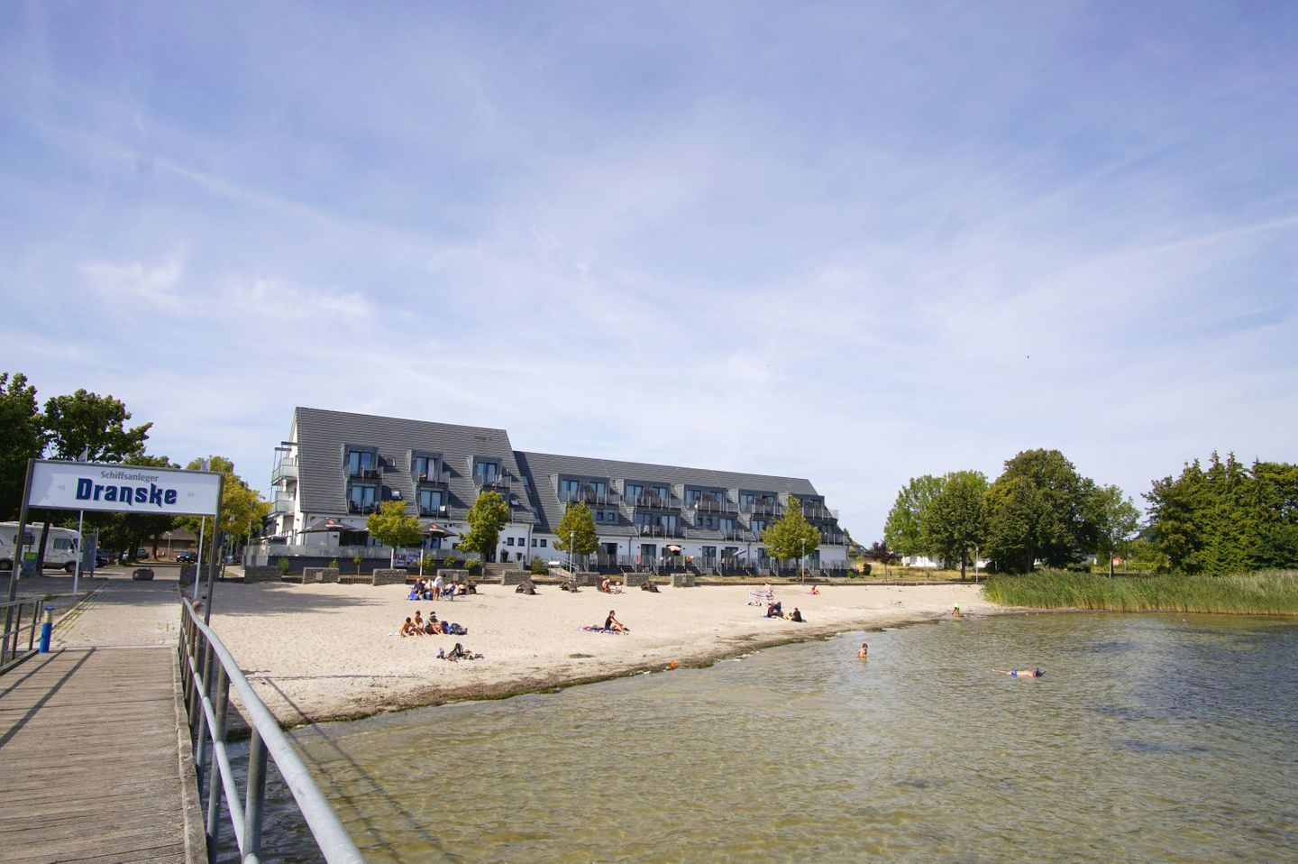 Ein Strandabschnitt mit einem Gebäude, auf dem 'Dranske' steht, und einer Holzpromenade.