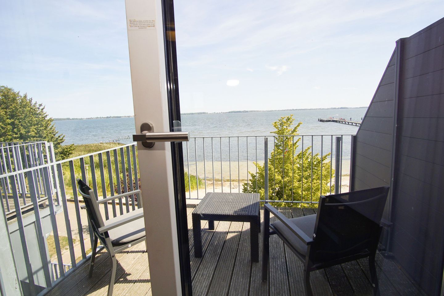 A balcony with a view of a body of water, a wooden deck, and a metal railing.