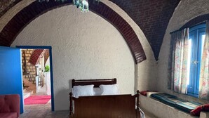 Una habitación con una cama, un sofá rojo, un ventanal con cortinas y un techo abovedado.