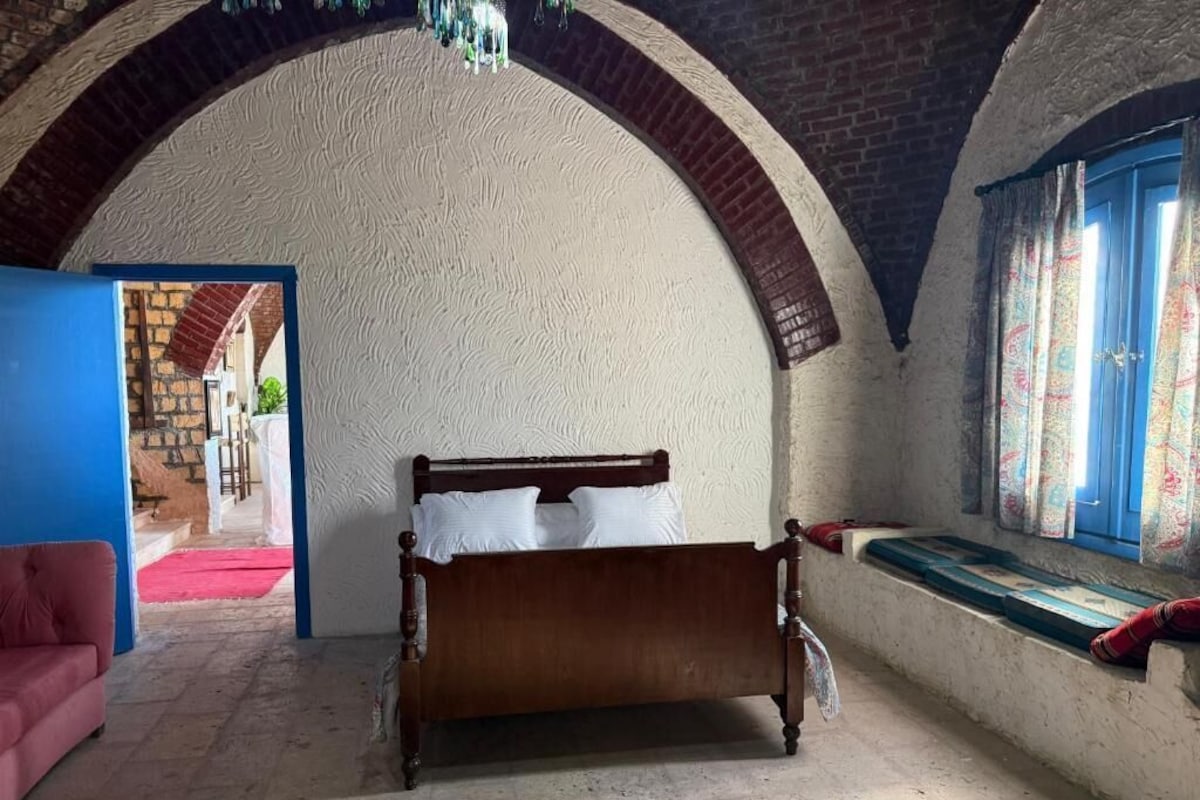 A room with a bed, a red sofa, a window with curtains, and an arched ceiling.