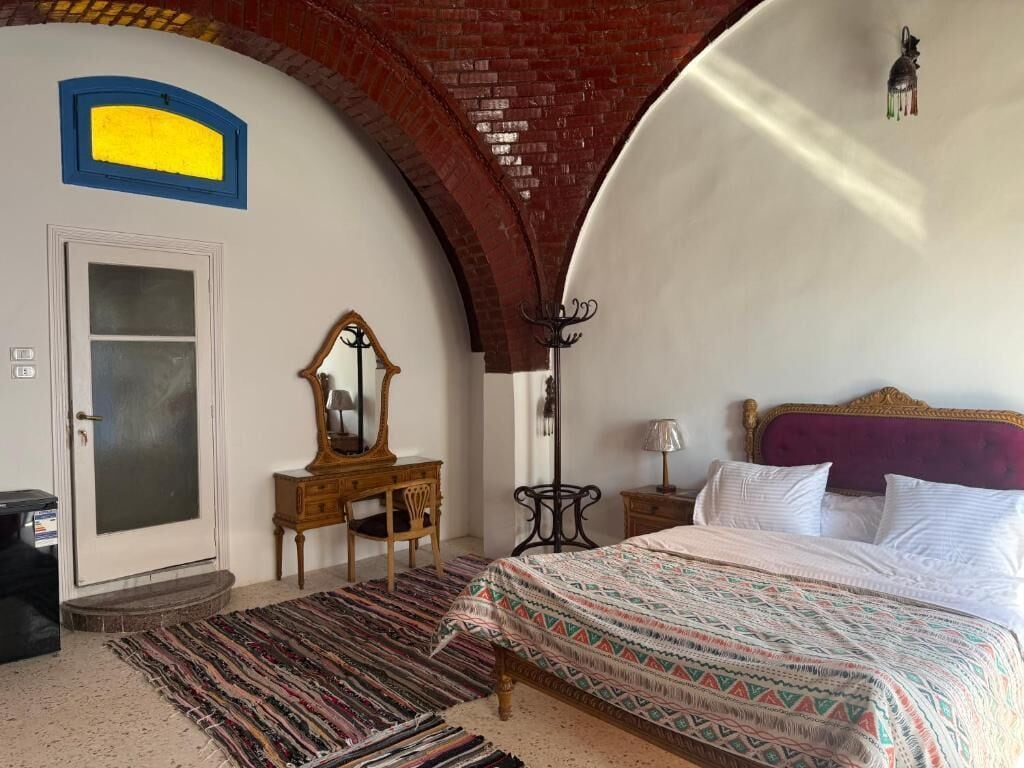 Un dormitorio con cama, cómoda, espejo, lámpara y puerta.