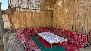 A room with a woven wall, a central table, and striped cushions.