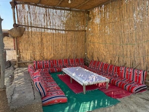 Una habitación con un muro tejido, una mesa central y cojines a rayas.
