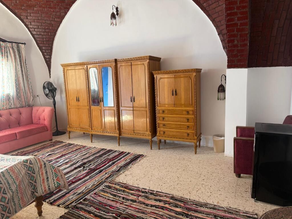 A room with a pink sofa, a wooden cabinet with drawers, a black TV stand, and a patterned rug.