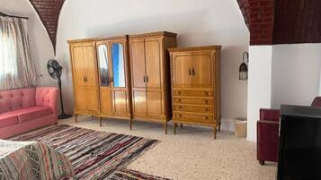 A room with a pink sofa, a wooden cabinet with drawers, a black TV stand, and a patterned rug.