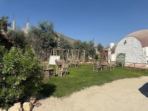 An outdoor seating area with wicker chairs and tables, surrounded by greenery and a white building with a dome-shaped roof. - VILLA EL SAFIR FARMHOUSE (Beheira Governorate)