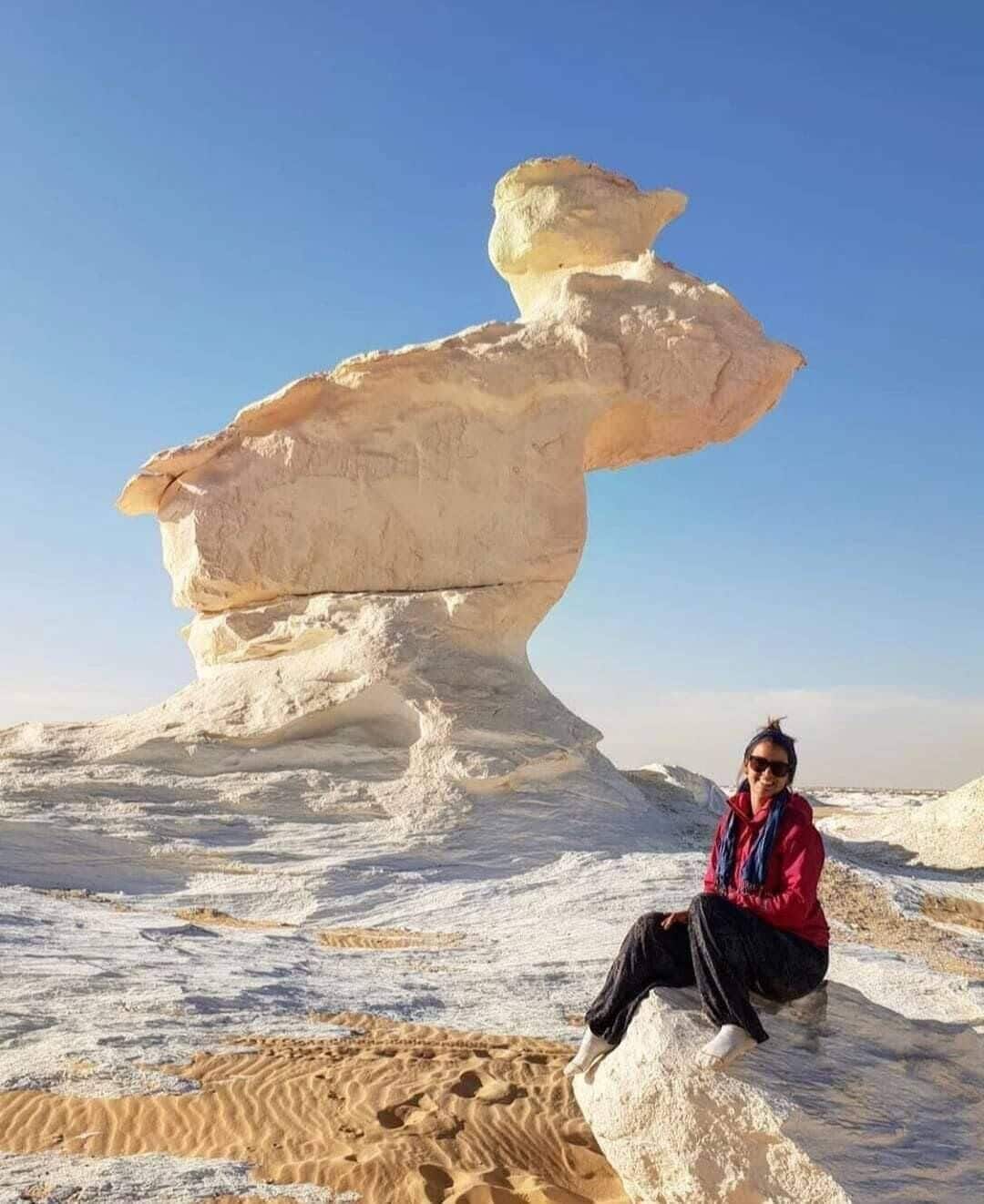A person sitting on a rock formation with a clear sky in the background.