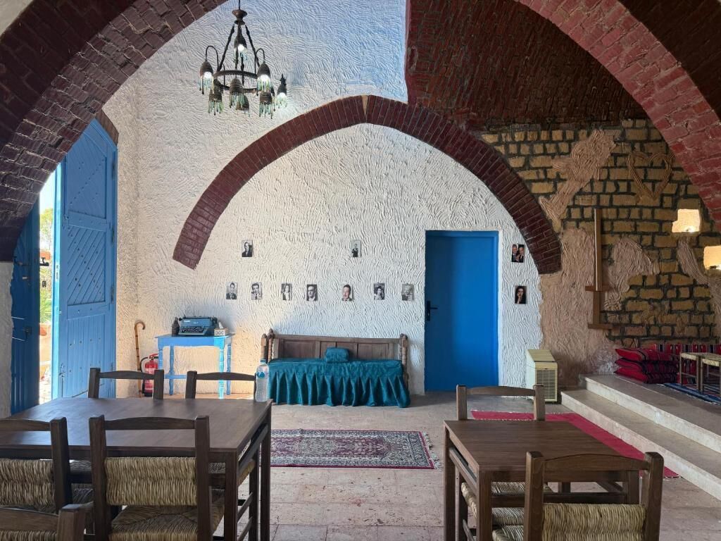 Una habitación con un techo alto abovedado, una cama con cabecera azul, una mesa de madera y una araña.