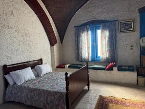 Un dormitorio con una cama, una ventana con cortinas, un reloj de pared y una mesita.