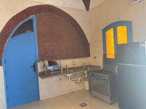 A kitchen with a blue door, a brick oven, and a black refrigerator.