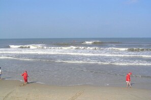 A beach with waves, people in red, and a clear sky. - Holiday apartment with 2 bedrooms (Petten)