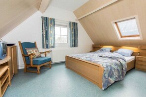 A bedroom with a sloped ceiling, a bed, a chair, a window with curtains, and a small table. - Holiday apartment with 2 bedrooms (Petten)