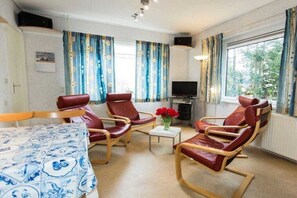A room with a bed, two leather chairs, a small table with flowers, a television, and curtains. - Holiday apartment with 2 bedrooms (Petten)