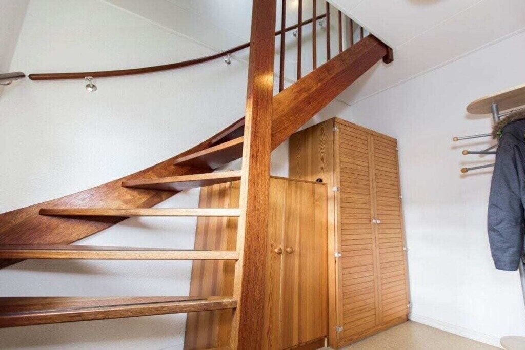 Una escalera de madera con barandilla, un armario de madera y un perchero con objetos.