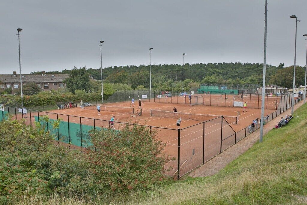 An outdoor tennis court with multiple players, surrounded by a fence and trees.